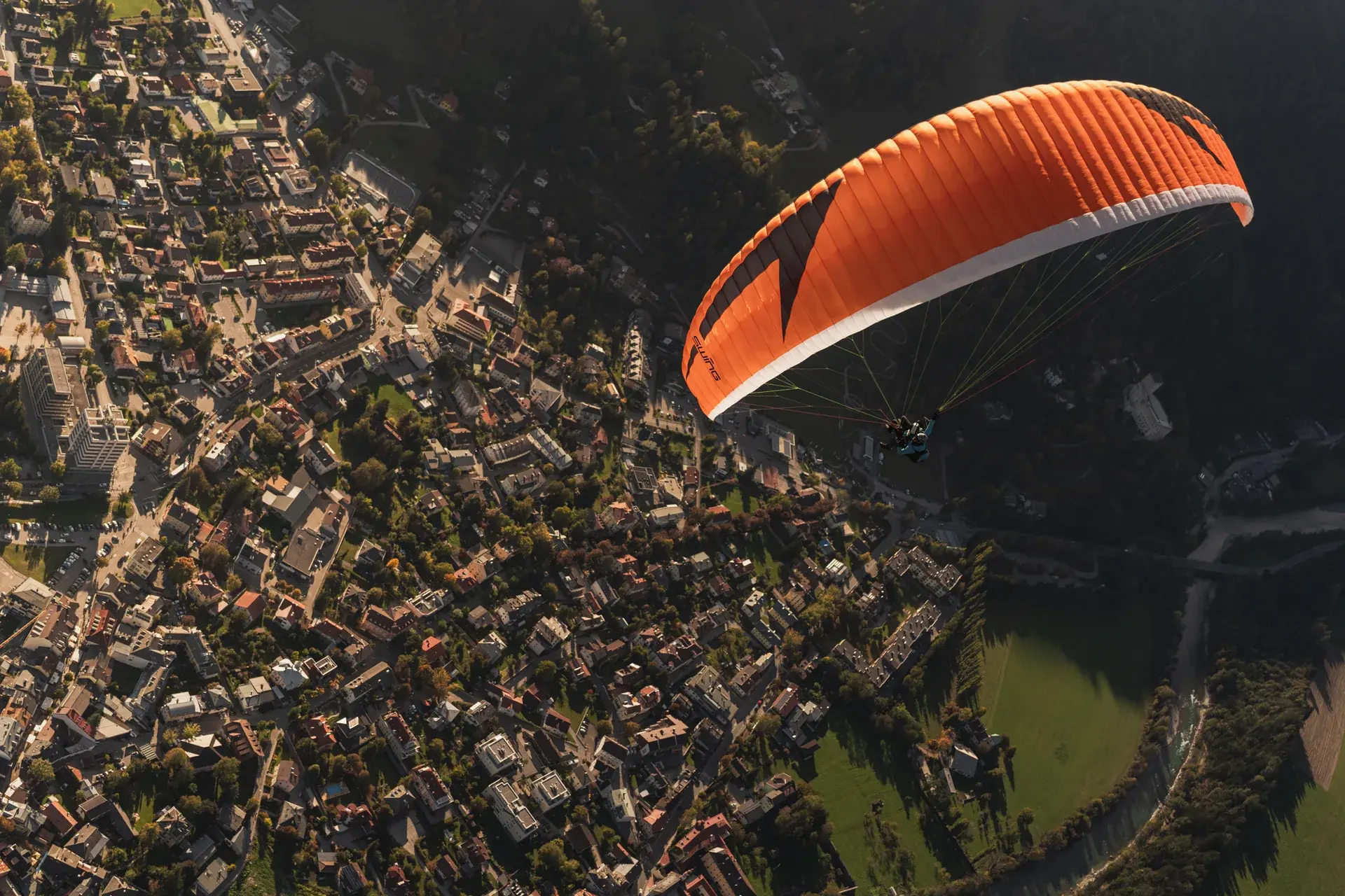 Tandemflug mit orangem Gleitschirm direkt über der Altstadt von Lienz in Osttirol