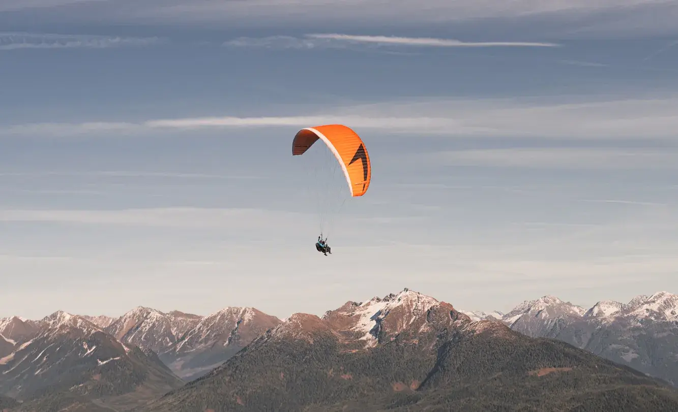 Tandem flight with an orange paraglider over Zettersfeld and the Lienz Dolomites in East Tyrol